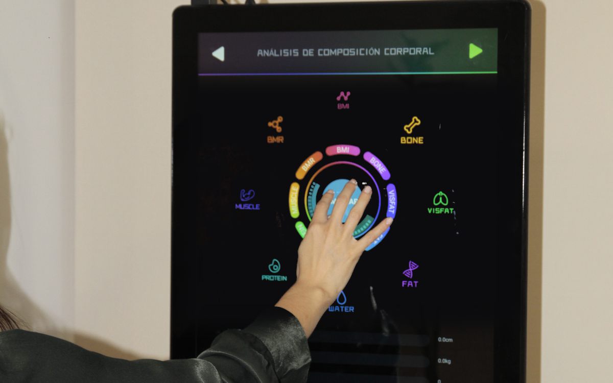 Mano pulsando la pantalla táctil del analizador Anovator, en el menú de análisis de composición corporal